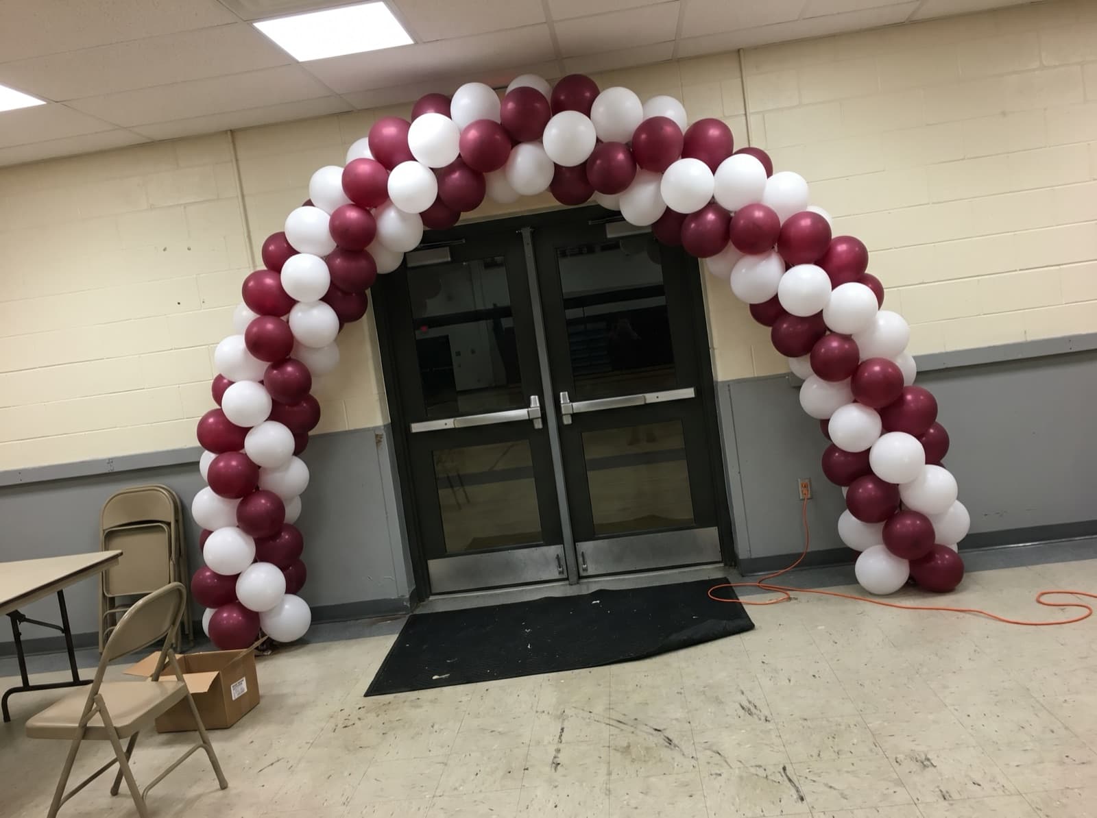 Spiral balloon arch in maroon and white over a gym entrance